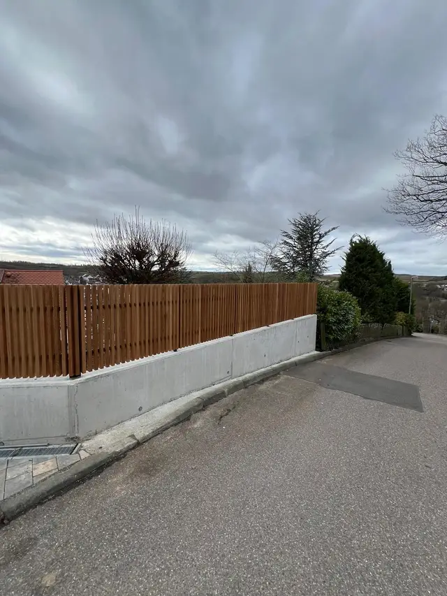 Zaun aus Stahl mit Holzlatten auf Betonsockel